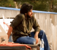 a man in a green shirt sits in front of a fence with a bottle of baby wipes in front of him