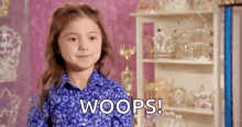 a little girl in a blue shirt is standing in front of a shelf with a shelf full of trophies .