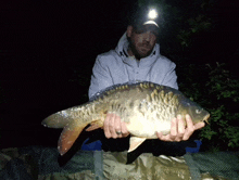 a man is holding a large carp in his hands at night