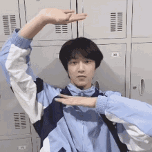 a young man is standing in front of a row of lockers making a heart shape with his hands .