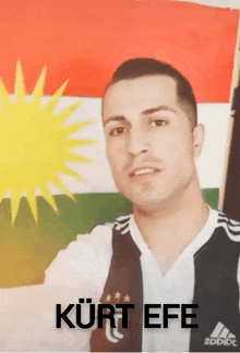 a man standing in front of a kurdish flag with the name kurt efe written on the bottom