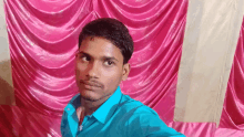 a young man in a blue shirt is standing in front of a pink curtain