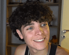 a young man with curly hair is smiling and wearing a necklace .