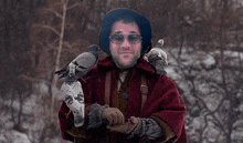 a man wearing glasses and a hat holds two pigeons on his shoulder