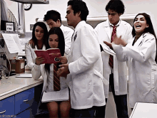 a group of people wearing lab coats and ties are standing around a table and one of them is holding a book