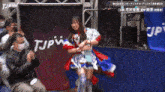 a woman in a red and blue dress is standing in front of a sign that says tjpw