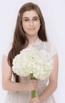 a woman wearing glasses is holding a bunch of white flowers