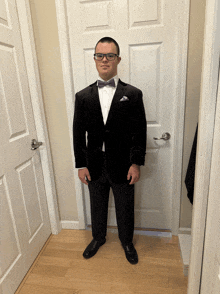 a man in a tuxedo and bow tie is standing in front of a door