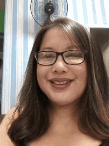 a woman wearing glasses is smiling in front of a wall fan