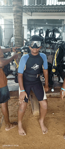 a young boy wearing a wetsuit and goggles stands in front of a palm tree