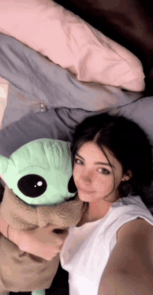 a woman is laying on a bed holding a stuffed green alien