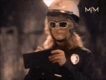 a woman wearing a helmet and sunglasses is holding a wallet in front of a sign that says mm