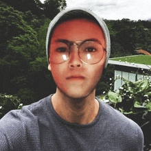 a man wearing glasses and a beanie takes a selfie with a green roof in the background