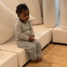 a baby is sitting on a white couch holding a toy