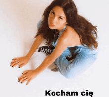 a woman in a blue jumpsuit is kneeling down with the words kocham cię written below her