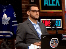 a man in a suit is sitting in front of a laptop with a toronto maple leafs jersey behind him