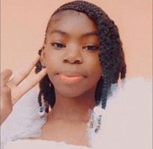 a young girl with braids in her hair is making a peace sign with her hand .