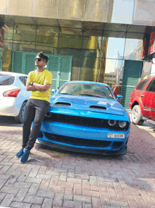 a man in a yellow shirt leans on a blue car with a license plate that says s2229