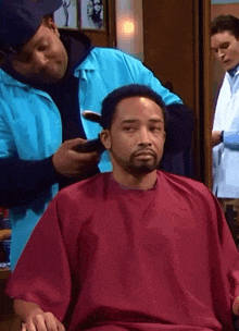 a man in a red shirt is getting his hair cut by a barber