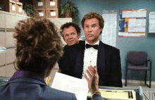 a man in a tuxedo is talking to a woman while another man stands behind him