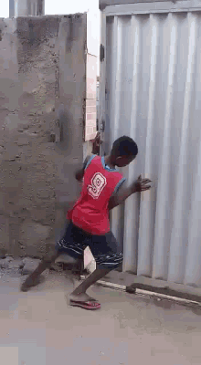 a young boy wearing a red jersey with the number 9 on it is standing in front of a white gate .