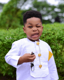 a young boy wearing a white shirt with gold buttons is holding a car key and smiling