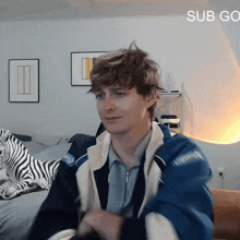 a man in a blue jacket is sitting on a couch with a zebra pillow behind him .