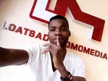 a man holds his finger to his mouth in front of a loatsado omomedia sign