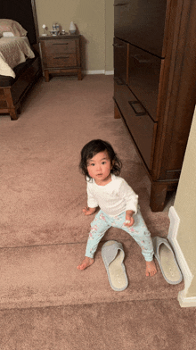 a little girl standing on a carpet next to a pair of slippers that say ' slippers ' on them