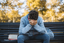 a young man sits on a bench with his head in his hands