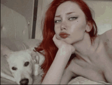 a woman with red hair laying on a bed with a white dog