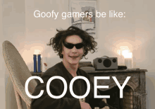 a man wearing sunglasses is sitting in front of a fireplace with the words goofy gamers be like cooey