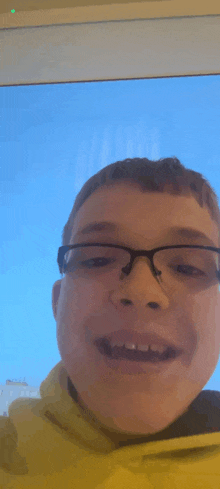 a young boy wearing glasses is smiling in front of a blue sky