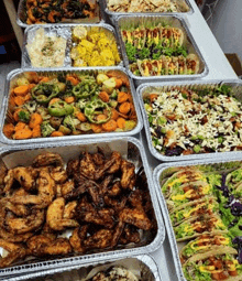 a table topped with trays of food including chicken wings , tacos , vegetables and salads .