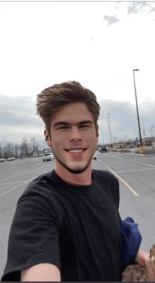 a young man in a black shirt smiles for the camera in a parking lot