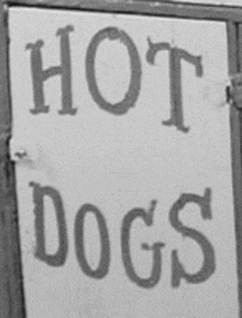 a black and white photo of a sign that says hot dogs on it .