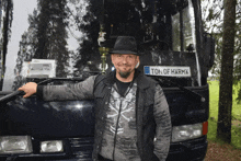 a man stands in front of a black van with a license plate that says ton of harma