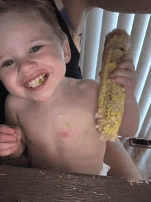 a baby is eating corn on the cob and smiling for the camera