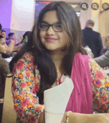 a girl wearing glasses and a floral shirt is smiling for the camera