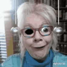 a woman wearing glasses and a blue sweater is making a funny face in front of a bookshelf .