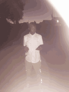 a man in a white shirt and khaki pants stands in a dark street