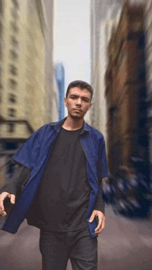 a man in a blue shirt and black t-shirt stands in a city street