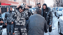 a man wearing a shirt that says " got seven mac 11 's bout " stands in front of a group of men