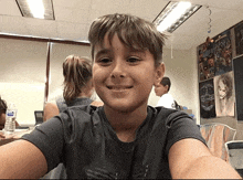 a young boy taking a selfie in a classroom with a bottle of aquafina water behind him