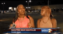 two women are standing next to each other in front of a news report about a shooting near a nightclub .