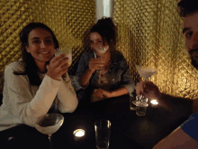 a group of people are sitting at a table toasting with martini glasses