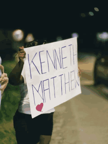 a woman holds a sign that says kenneth matthew