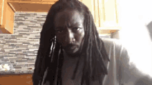 a man with dreadlocks and a beard is making a funny face .