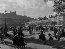 a black and white photo of people sitting at tables in a park with a castle in the background .