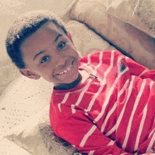 a young boy is laying on a couch wearing a red shirt and smiling .